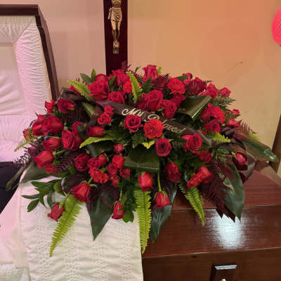 Large red rose funeral spray on a casket with a memorial ribbon