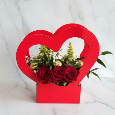 Red roses arranged in a heart-shaped gift box with gold chocolates