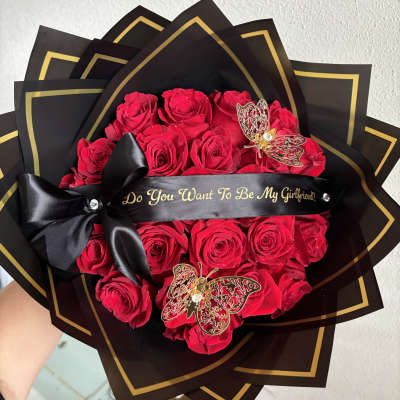 Red roses wrapped in black paper with gold trim and a black ribbon