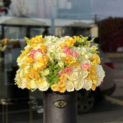Large bouquet of white, yellow, and pink roses in a black hat box