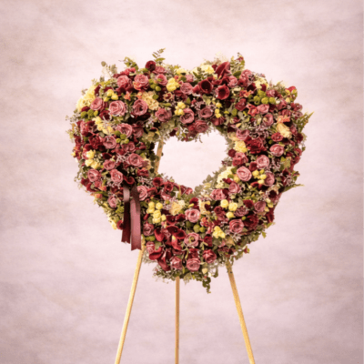 Heart-shaped standing wreath of mauve and yellow flowers on a wooden easel stand