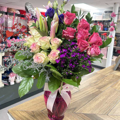 Mixed bouquet of pink roses, lilies, and purple flowers in a pink vase