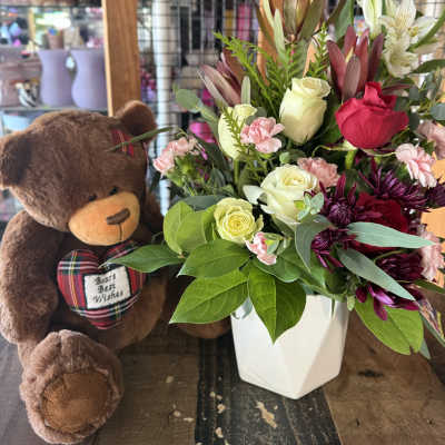 Bouquet of roses and chrysanthemums in a white vase beside a teddy bear