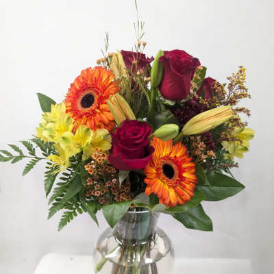 Bouquet of red roses, orange gerbera daisies, and yellow alstroemeria in a glass vase