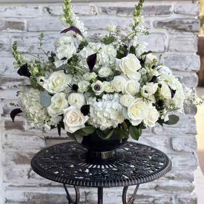 White floral arrangement in a black vase with dark accent blooms
