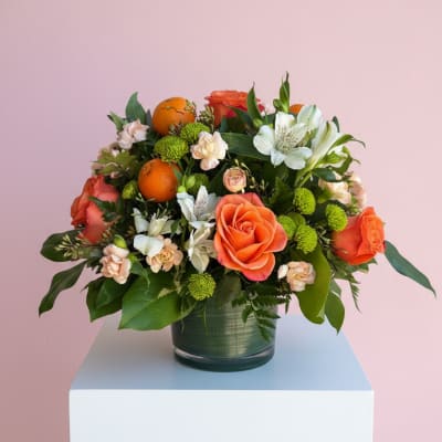 Orange roses and white alstroemeria in a glass vase with oranges