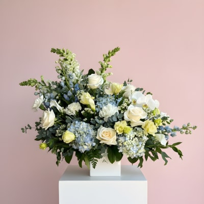 Large white and pale blue floral arrangement in a white vase