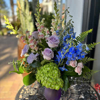 Bouquet of lavender roses, blue delphinium, and green hydrangea in a purple vase