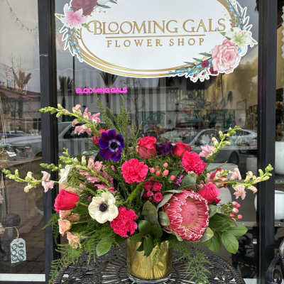 Bright mixed flower arrangement in a gold vase on a metal table