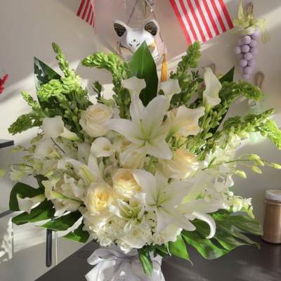White lilies and cream roses in a white basket with a ribbon
