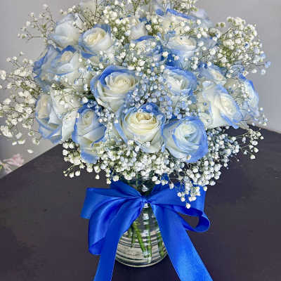 Blue-tinted white rose bouquet in a glass vase with baby's breath and a blue ribbon