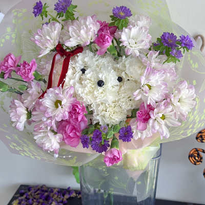 Bouquet of white, pink, and purple flowers in clear wrap with a red ribbon