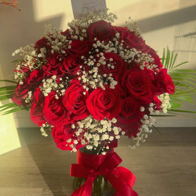 Bouquet of red roses with white baby's breath in a glass vase and red ribbon