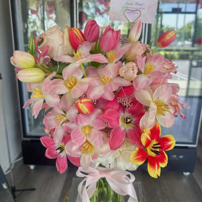 Pink and white tulips with pale blossoms in a glass vase tied with a ribbon
