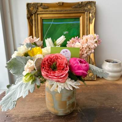 Small mixed arrangement of pink, white, and yellow flowers in a ceramic vase on a wooden table.