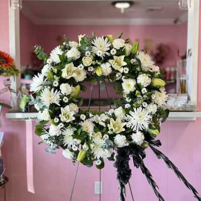 White floral wreath on a stand with black ribbon streamers