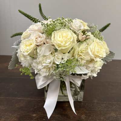 Cream rose and hydrangea arrangement in a square glass vase with a white ribbon