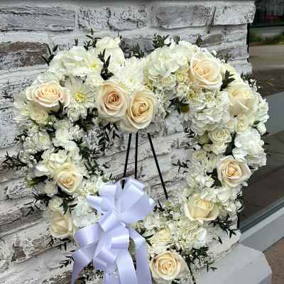 Heart-shaped white floral wreath with cream roses and a lavender ribbon on a stand