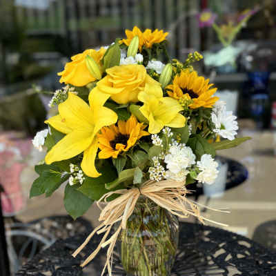 Yellow bouquet with sunflowers, roses, and white flowers in a glass vase
