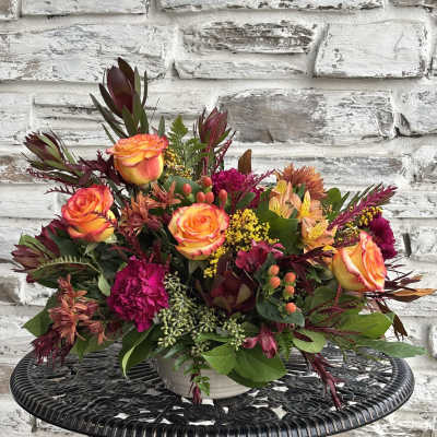 Mixed bouquet of orange roses and magenta flowers in a white vase