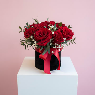 Red roses arranged in a black hatbox with a red ribbon