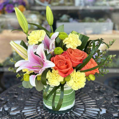 Bouquet of pink lilies, coral roses, and yellow carnations in a glass vase