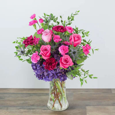 Pink roses and carnations in a clear glass vase with purple hydrangea