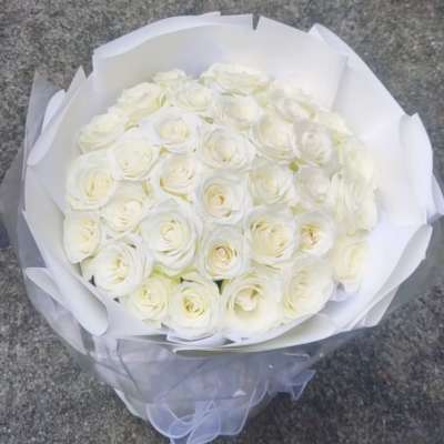 Bouquet of white roses wrapped in white paper with a sheer ribbon
