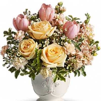 Compact arrangement of peach roses and pink tulips in a white ceramic urn-style vase