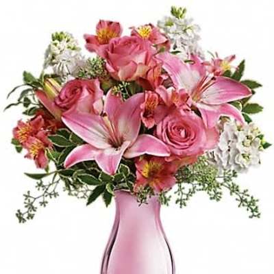 Pink and white bouquet of lilies and roses arranged in a pale pink glass vase