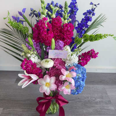 Tall bouquet of pink, blue, purple, and white flowers in a glass vase