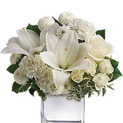 Compact white lilies, roses, carnations, and mums in a clear glass cube vase.