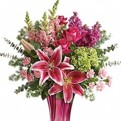 Tall pink and green bouquet with lilies, roses, and snapdragons in a pink glass vase.