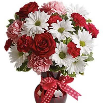 Red, white, and pink bouquet of roses, daisies, and carnations in a red vase with a polka dot bow.