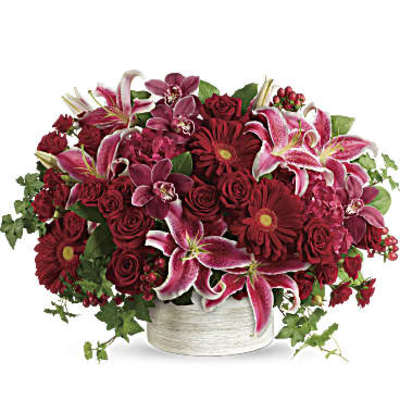 Low arrangement of red roses, gerbera daisies, and pink lilies in a white ceramic container