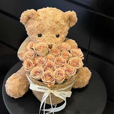 Teddy bear holding a heart-shaped box of peach roses