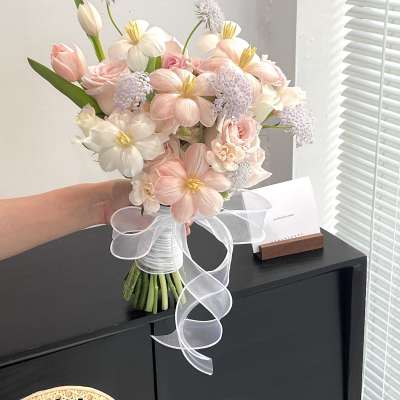 Handheld bouquet of pale pink and white flowers tied with a white ribbon