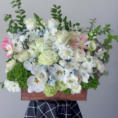 White floral arrangement with orchids and roses in a wooden box