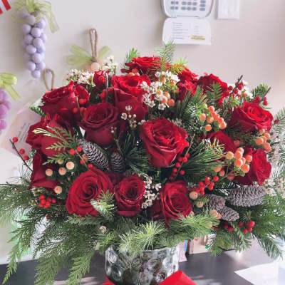 Red rose arrangement in a glass vase with pinecones and a red ribbon