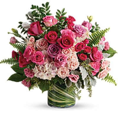 Rounded arrangement of pink and red roses in a leaf-wrapped glass cylinder vase