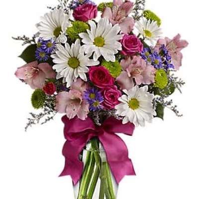 Mixed bouquet of white daisies, pink roses, and purple accents in a clear vase with a pink bow