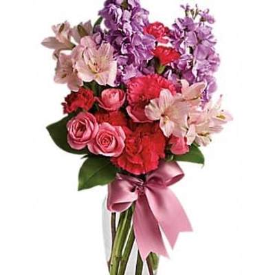 Pink and purple mixed flower arrangement with roses, carnations, and alstroemeria in a glass vase with a pink bow