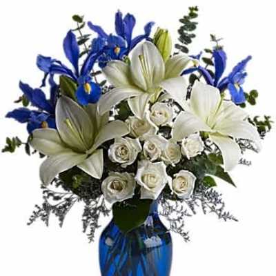 Arrangement of white lilies, white roses, and blue irises in a cobalt blue glass vase