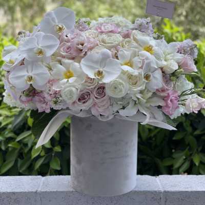 White orchids and blush roses arranged in a tall gray vase