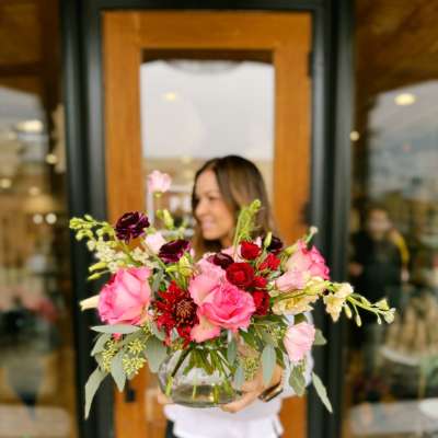 Woman holding a mixed bouquet of pink and red flowers in a glass vase