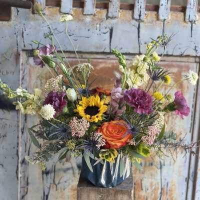 Mixed bouquet with a sunflower, orange rose, and purple blooms in a vase