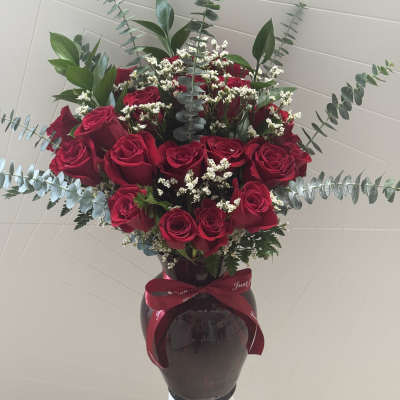 Bouquet of red roses in a dark vase with eucalyptus and white filler flowers