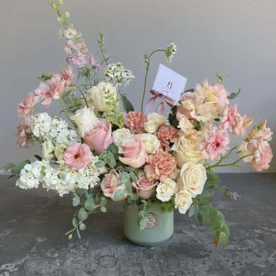 Pastel floral arrangement in a green vase with roses and mixed blooms