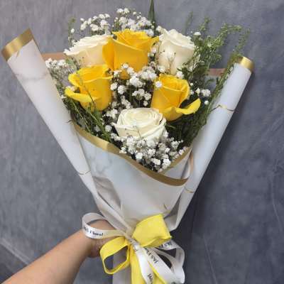 Bouquet of yellow and white roses wrapped in white paper with a yellow ribbon