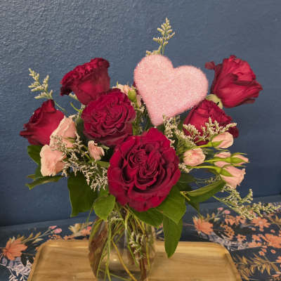 Red and blush roses in a glass vase with a pink heart pick